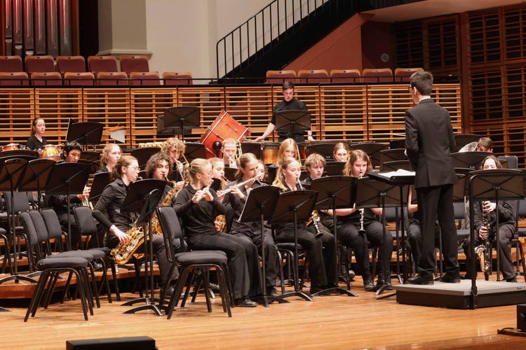 Image of one of our school bands performing on stage at the Sydney Conservatorium of Music. They are in playing position with their conductor standing at the front on a podium.
