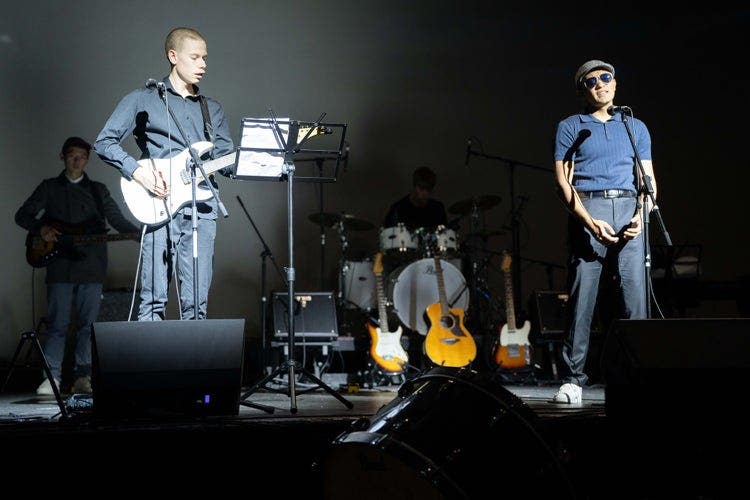 Image of three students - a singer, guitarist and bassist who are performing on stage under LED lights as part of a band.