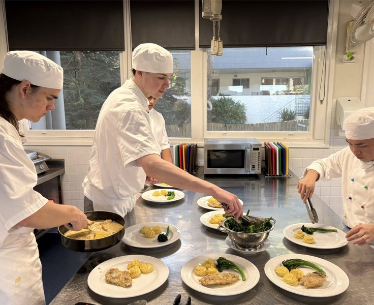 An image of three of our VET Hospitality Cookery students as they plate up their dishes.