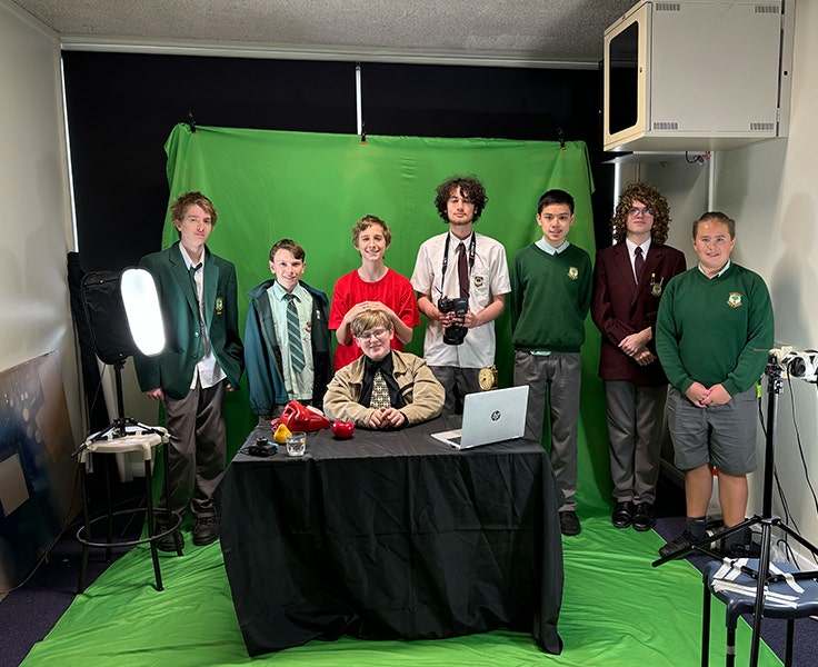 An image of eight of our photography and digital media students holding cameras and standing in front of a green screen.
