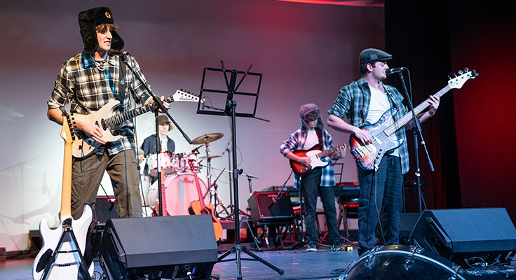 Four members of a band performing music on stage at our Music and Drama Night including two electric guitars, bass and drums.