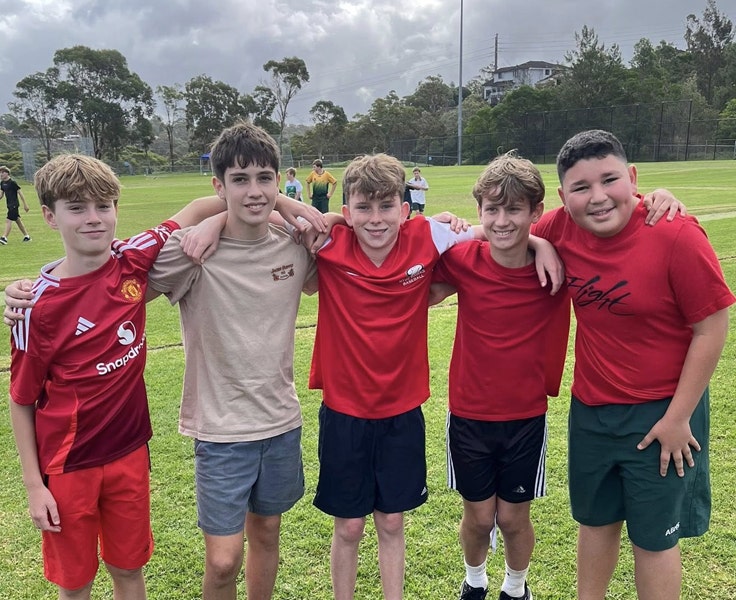 Five students huddled in a group and smiling on the oval at the school's Athletics Carnival.