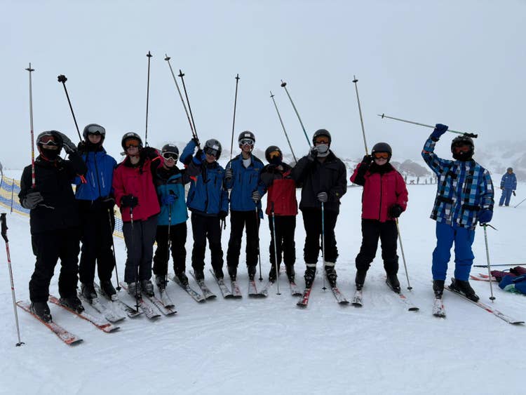 A group of students standing on the snow field raising their ski poles into the air.