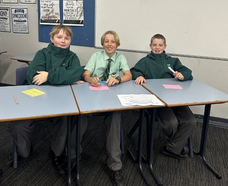Image of three students writing notes for the debating excursion.